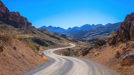 Winding dirt road through arid desert landscape under bright blue sky in southern Nevada during daylight hours