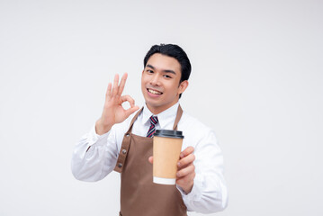 A smiling barista gives an OK gesture while holding a takeaway coffee cup, confidently recommending the drink. Isolated on a white background.