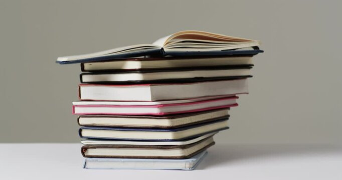 A stack of various hardcover and paperback books sits against a neutral background, with copy space