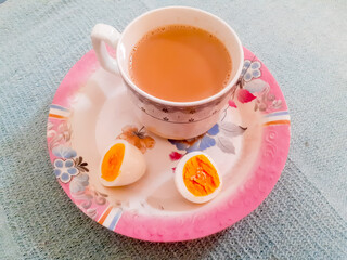 Cut egg slices and hot tea cup on plate, isolated on abstract background 