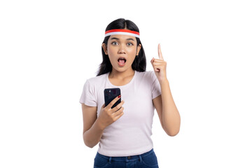 Surprised young Asian woman holding smartphone and pointing up isolated on white background. Indonesian Independence Day Celebration Concept