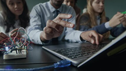 Stab shot of unrecognizable Black male programming teacher typing on laptop keyboard while explaining material to multiethnic group of gen z schoolkids during lesson - Powered by Adobe
