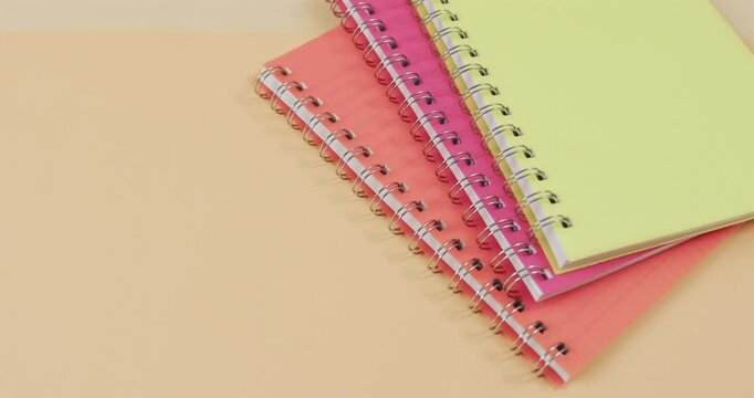Colorful spiral notebooks are stacked on a dual-toned pink and yellow background, with copy space