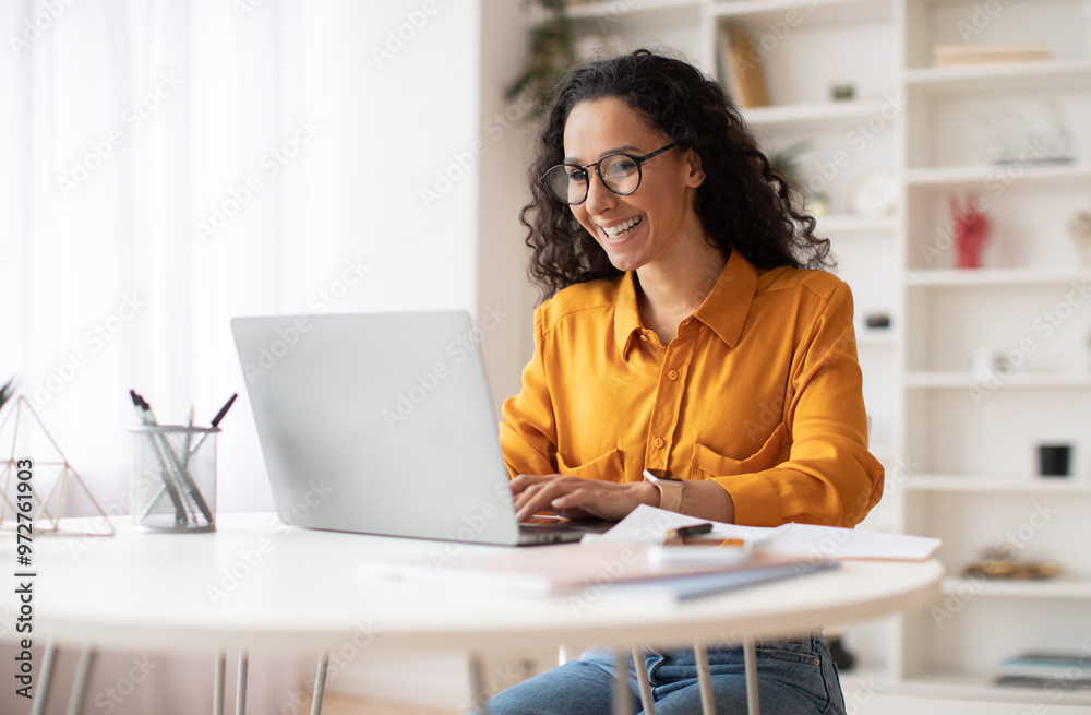 Poster happy middle eastern businesswoman using laptop typing and working online sitting at workplace weari