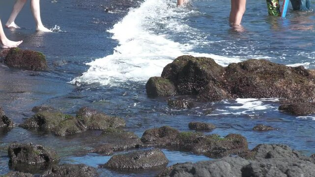 Waves gently rolling to a rocky beach, with people wading in the water