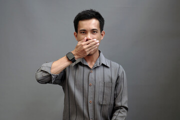 A young man covered his mouth with his hand, as if holding himself back from speaking. His facial...