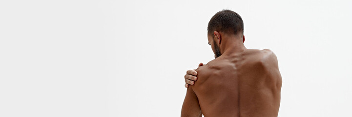 Naklejka premium Banner. Rear view of man holding hand on shoulder as he feels pain in joints against white background with negative space. Concept of beauty and fashion, style and youth, male health.
