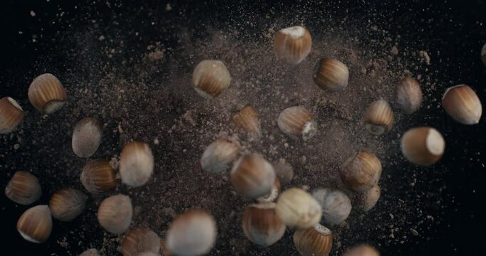 Super slow motion macro of flying raw bio organic chocolate cocoa powder splash with unshelled hazelnuts isolated on dark background at 1000 fps.