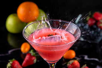 Cocktail glass with fresh fruits, apples, strawberries, kumquats and blueberries making a splash with the liquid flying