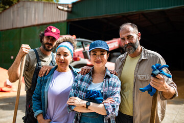 Group portrait of diverse farmers standing together in front of a tractor in the farmyard