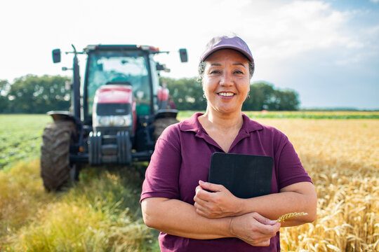 Portrait of a smiling middle aged female farmer on wheat field holding tablet