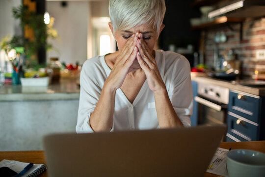 Stressed senior woman working on laptop in modern kitchen