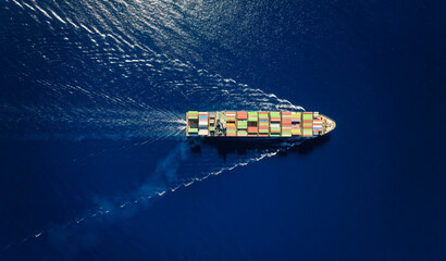 High aerial overhead view of a large industrial container cargo vessel sailing over the ocean with speed