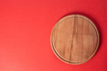 Round wooden cutting board on a red background. Top view. Copy space.