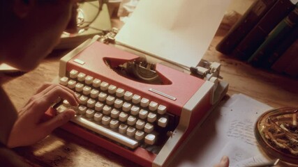 Talented writer typing on vintage typewriter at desk with books, papers, ashtray and landline phone in soft glow light. Over-the-shoulder view