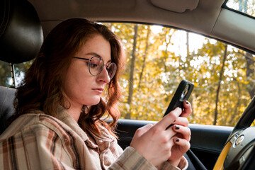 Girl driving a car. Girl using phone. Gadgets. Beautiful girl in a car. Red-haired. Young driver. Confident girl driving a car. Girl on the phone