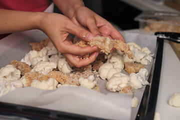 A person s hands preparing a baking tray with cauliflower florets and breaded chicken pieces, ready for the oven. Emphasizes the blend of fresh vegetables and protein for a balanced diet.