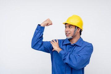 An asian worker in blue coveralls and a yellow hard hat flexes his bicep, showcasing strength and confidence.Themes of physical ability, hard work, and resilience