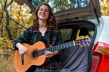 Young teenage girl playing guitar. Girl playing guitar in car. Autumn atmosphere. Car trip....