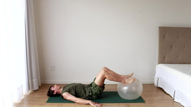 homem faz exercicios fis&iacute;cos e alongamentos com bola de pilates 