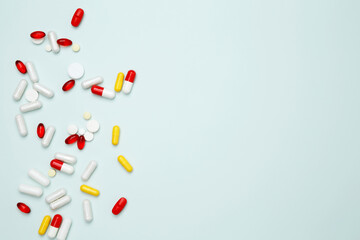 Various colorful pills and capsules scattered on a light blue background. Concept of medicine, healthcare, and pharmaceutical industry