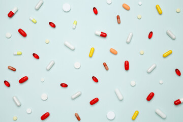 Various colorful pills and capsules scattered on a light blue background. Concept of medicine, healthcare, and pharmaceutical industry
