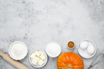 Baking ingredients including flour, butter, sugar, spices, eggs and pumpkin arranged on a gray background. Seasonal autumn baking