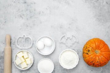 Baking ingredients including flour, butter, sugar, spices, eggs and pumpkin arranged on a gray background. Seasonal autumn baking