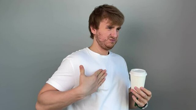 young handsome man in white t-shirt spilled coffee on his t-shirt. concept stained and dirty clothes, spot, gray background