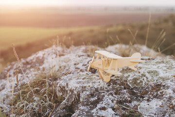 Vintage Wooden Airplane Model on Rock Overlooking Scenic Countryside at Sunset