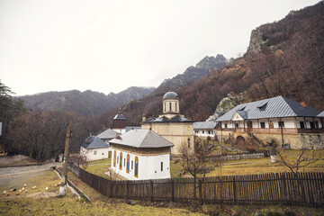 Fototapeta premium Amidst majestic mountains, a historic monastery reveals its beauty under soft clouds, surrounded by nature's tranquility, inviting quiet reflection and exploration