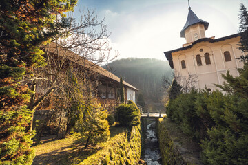 In the early morning light, a serene monastery unfolds, surrounded by lush greenery and gentle streams, offering a peaceful retreat amidst the Carpathian Mountains