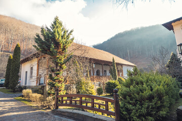 A picturesque house stands in the mountains, basking in sunlight. Lush green trees frame the peaceful surroundings, creating a tranquil escape into nature