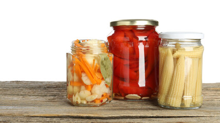 Different pickled products in jars on wooden table against white background