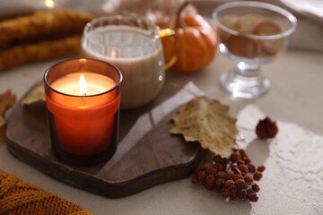 Burning candle on light textured table, closeup. Autumn atmosphere