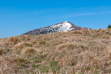 Scenic hiking trail over dry alpine meadows and rolling hills to snow-capped mountain peak Lenzmoarkogel, Gleinalpe, Lavantal Alps, Styria, Austria. Wanderlust in wilderness of Austrian Alps in spring