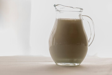 Sunlit Crystal Jug Filled with Milk on White Background.