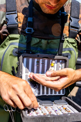 Fisherman selecting fly fishing lures from tackle box