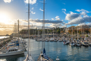 A stunning view of a Funchal marina on Madeira island filled with boats, yachts and sailboats under a beautiful sunset in a lively coastal city