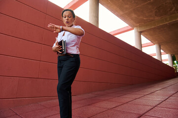 Professional woman rushing through corridor while checking time and holding documents