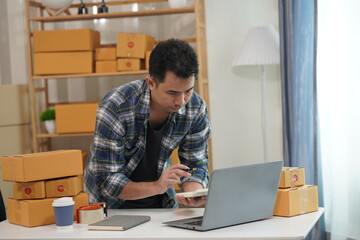 Small business owner starting up using smartphone and writing address on package box to send to...