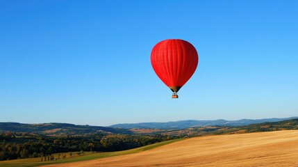 A bright red hot air balloon floating in a clear blue sky, casting a shadow on the landscape below.