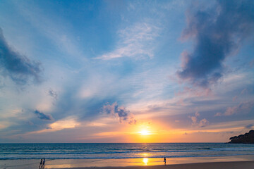 Fototapeta premium A stunning sunset over the ocean with soft golden light reflecting on the water, featuring silhouettes of people walking along the shore. Water flows from a small stream into the sea.