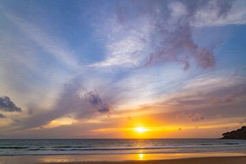 A stunning sunset over the ocean with soft golden light reflecting on the water, featuring silhouettes of people walking along the shore. Water flows from a small stream into the sea.
