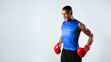 Angry Fighter. Aggressive black sports man in boxing gloves screaming over yellow background,...