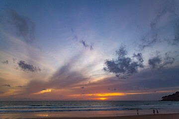 A serene beach scene at dusk, showcasing a vivid sunset with colorful clouds reflected on the calm waters and wet sand. amazing sky in sunset over Karon beach Phuket. sweet sky background.
