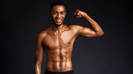 Athletic Man's Torso. Happy afro fitness model showing shoulder muscles, strong hands, chest and biceps over black wall