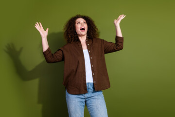 Portrait of nice young girl raise arms look up empty space wear brown shirt isolated on khaki color...