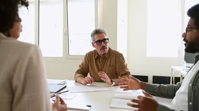 Mature grey-haired professional man in a shirt listening to a colleague attentively during an office discussion, representing a supportive and constructive business dialogue and friendly atmosphere