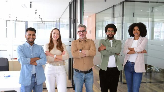 A vibrant team of five professionals stands with confidence in office, arms crossed and smiles wide, representing the epitome of a diverse and dynamic workgroup poised for collaboration and success